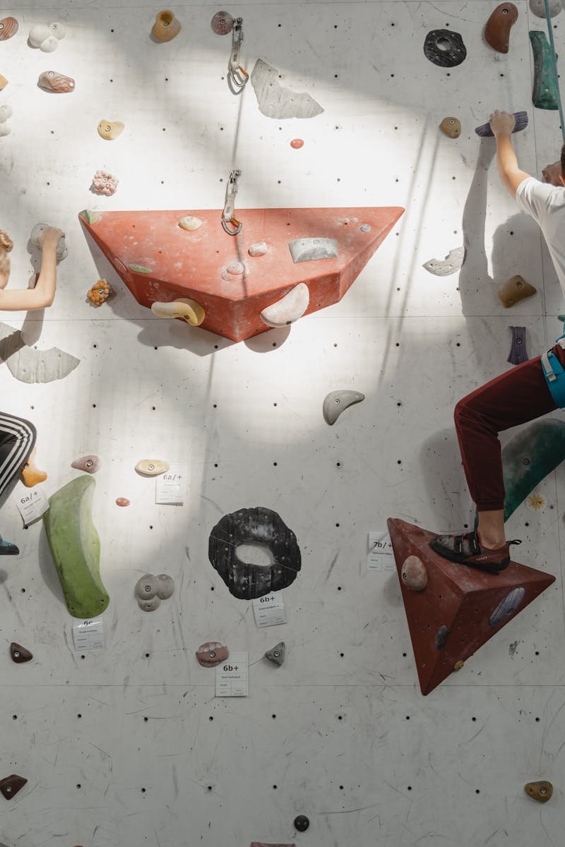 Two young climbers ascend an indoor rock wall, focused and determined.